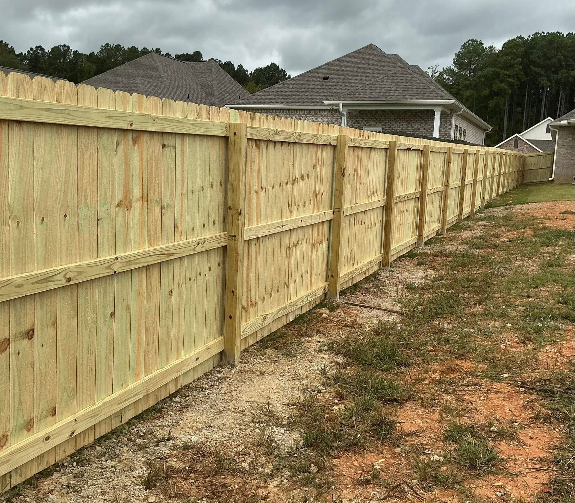 New wooden privacy fence along a grassy backyard beside suburban houses under cloudy skies