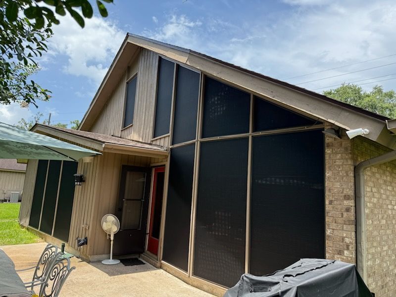 Exterior of a house with large black screens covering windows, likely for sun protection. Beige siding and a brick exterior.