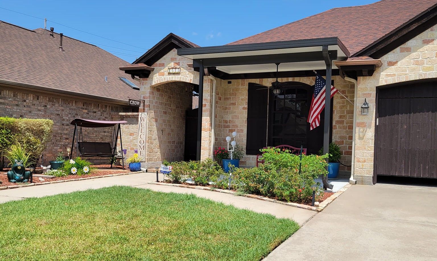 A brick house with a small porch and American flag. The yard has a grassy lawn and a walkway.