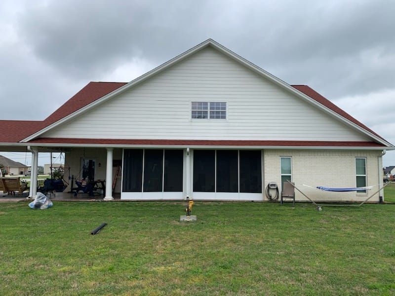 Back of a white house with red roof and screened porch; a hammock hangs in the grassy yard on an overcast day.