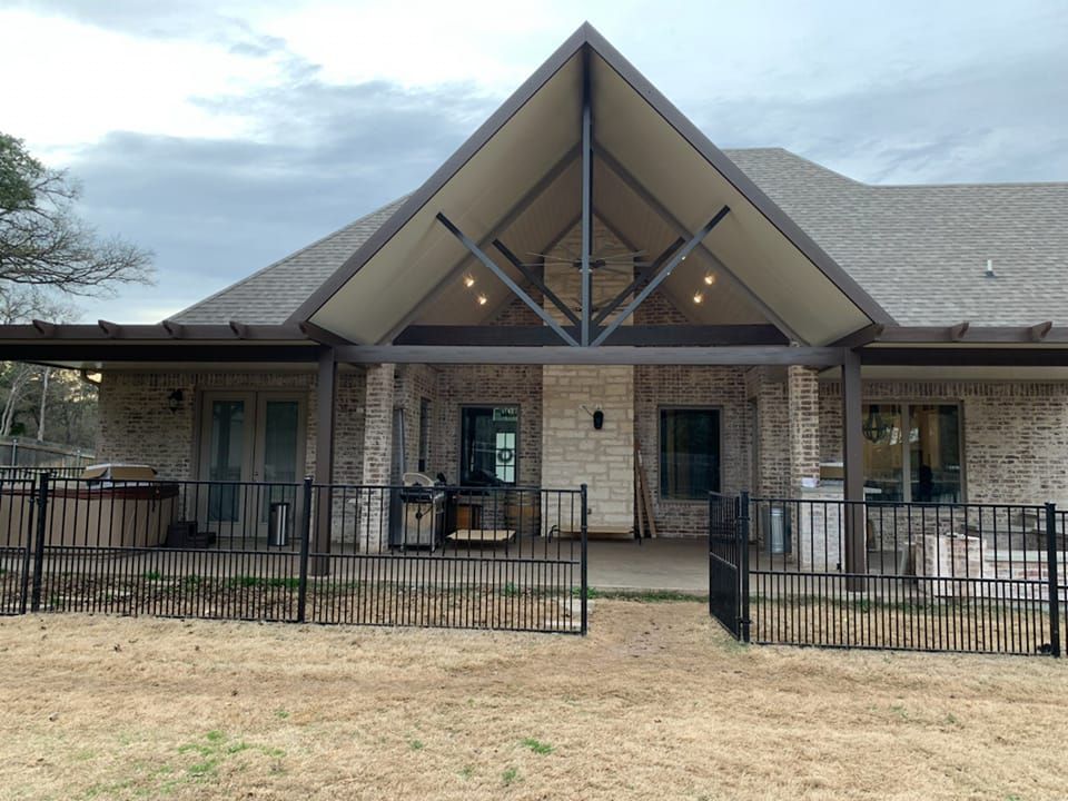 Backyard with a covered patio. Brick house with a black metal fence in front. Cloudy sky.