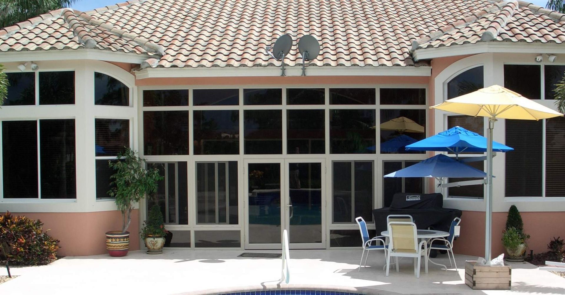 Back patio with a pool, featuring a seating area under two umbrellas, and a large glass-walled structure.