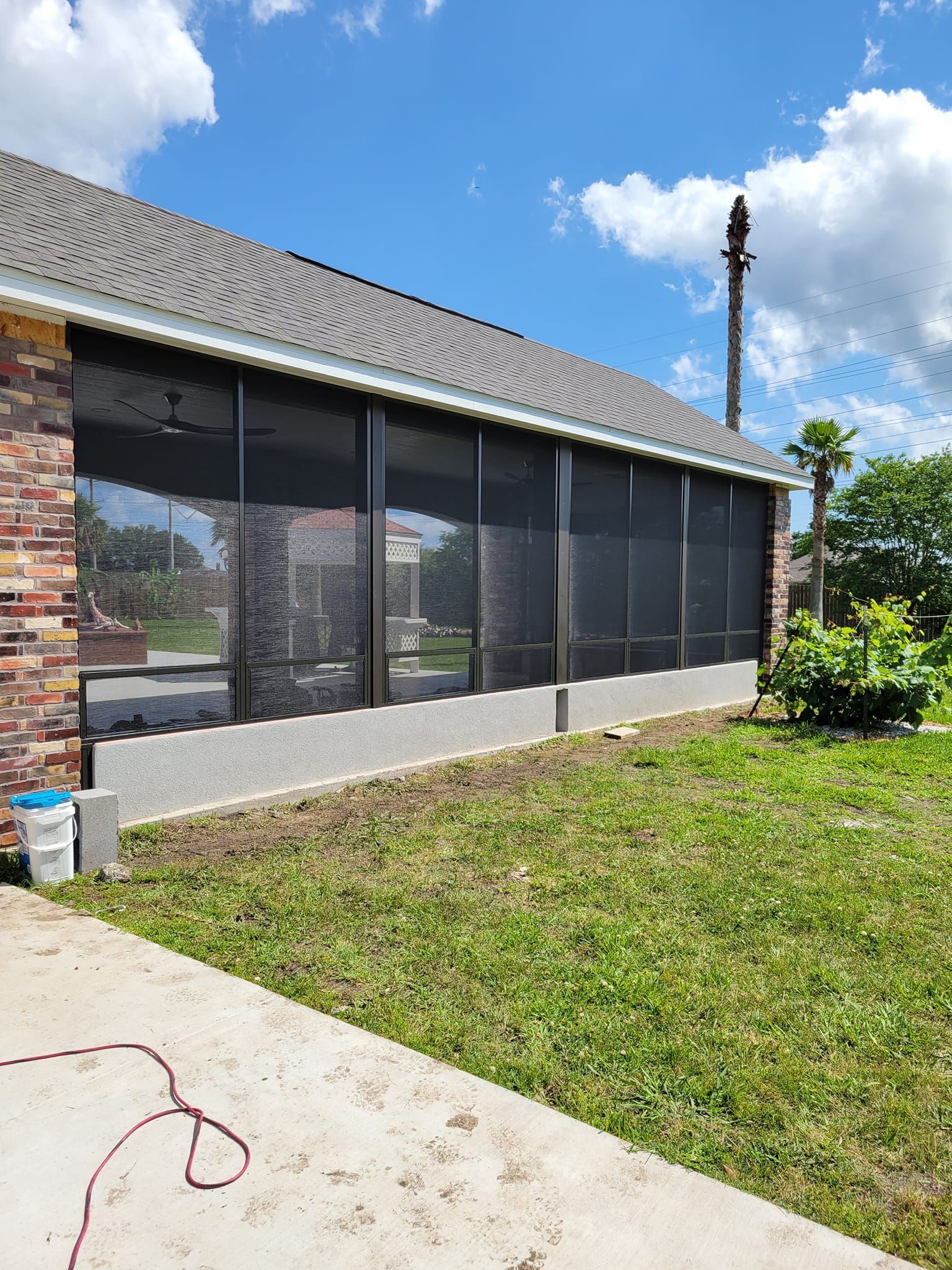 Screened-in porch attached to a brick home with a gray roof, overlooking a yard with green grass and a clear blue sky.