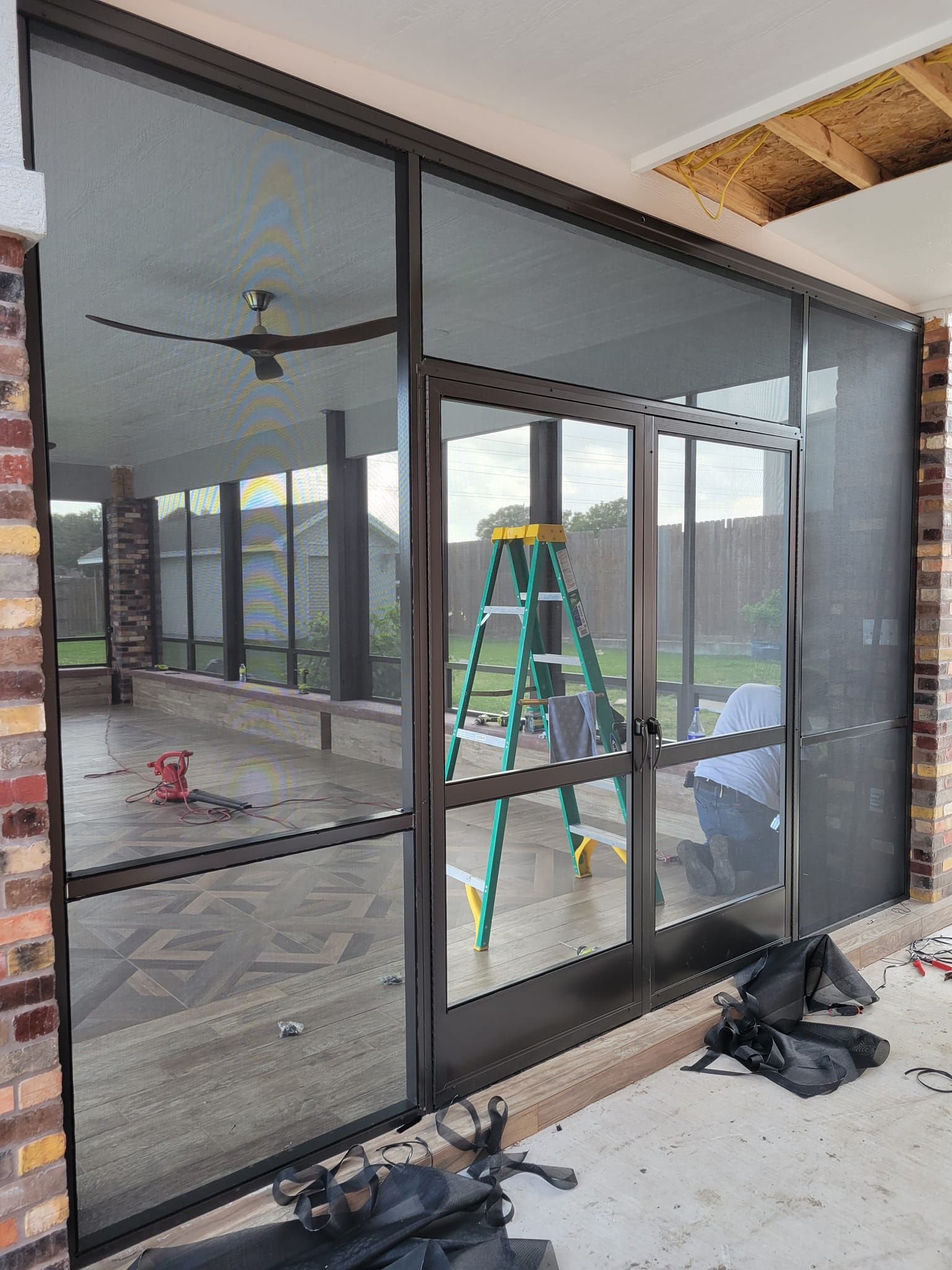 Screened-in porch with a brick exterior, dark-framed screen doors, and a green ladder inside.