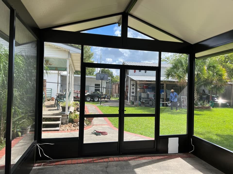 View from inside a screened-in porch looking out into a backyard with a lawn, trees, and a house.