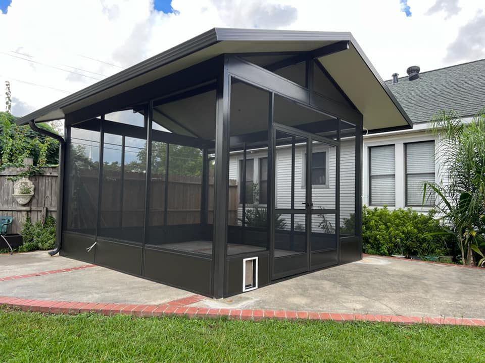 Black screened-in patio enclosure with a sloped roof, set on a concrete patio and surrounded by a yard.