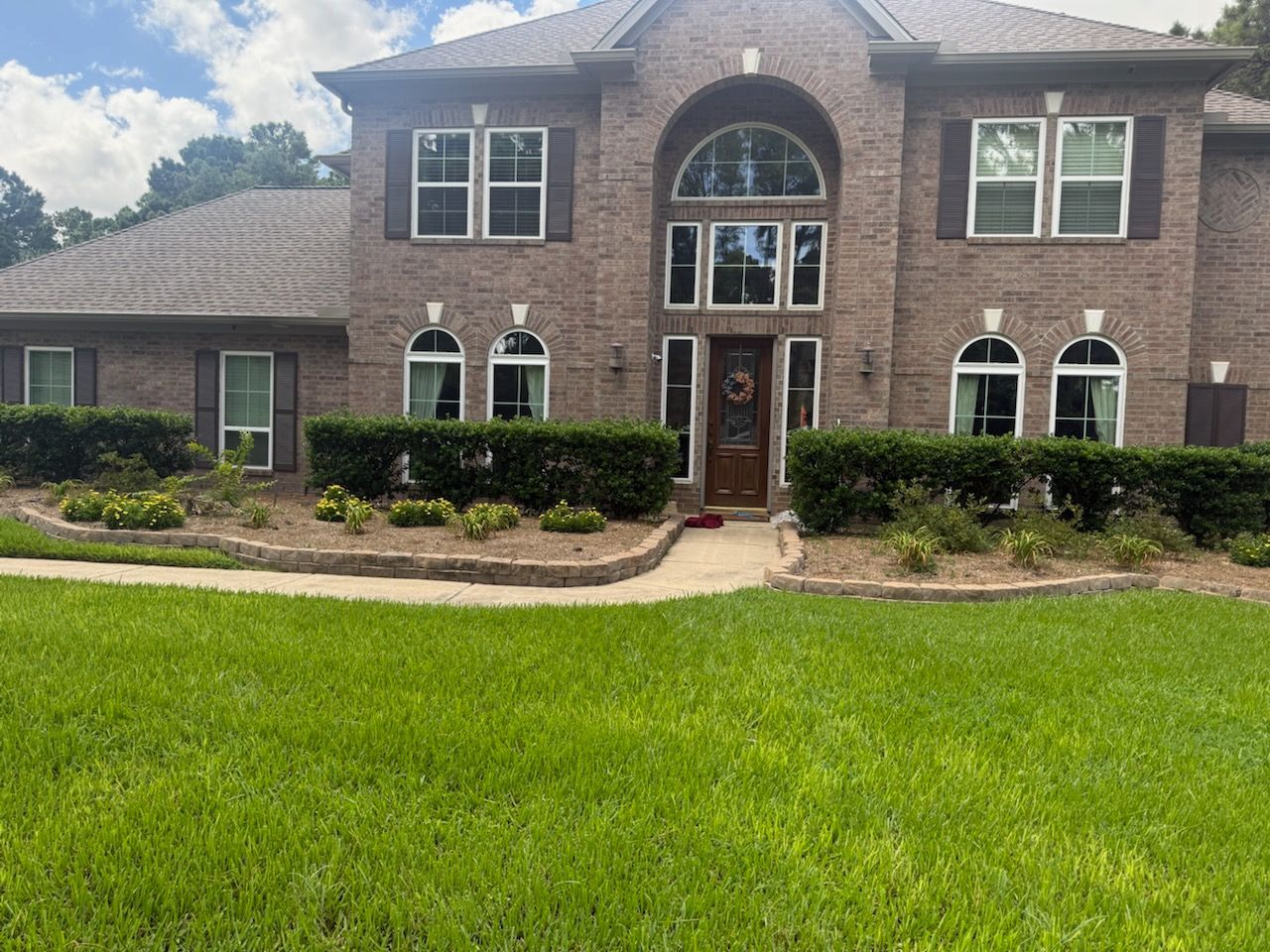 Two-story brick house with a manicured lawn, shrubs, and a dark brown door; clear sky.