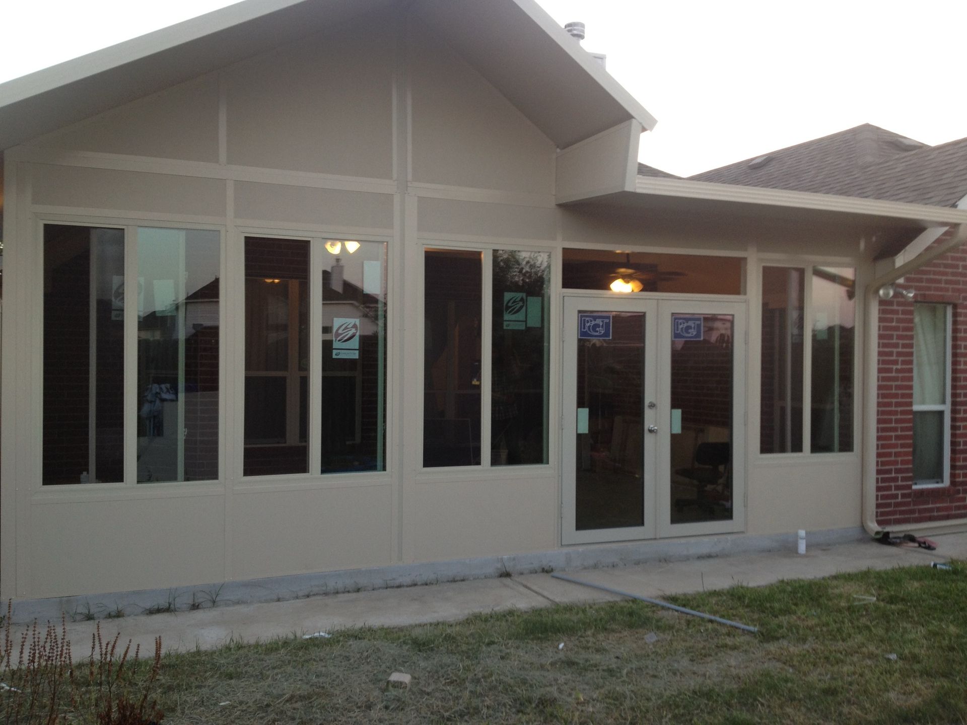 Sunroom addition on a house with large windows and double doors. Beige siding with a concrete patio and brick exterior.