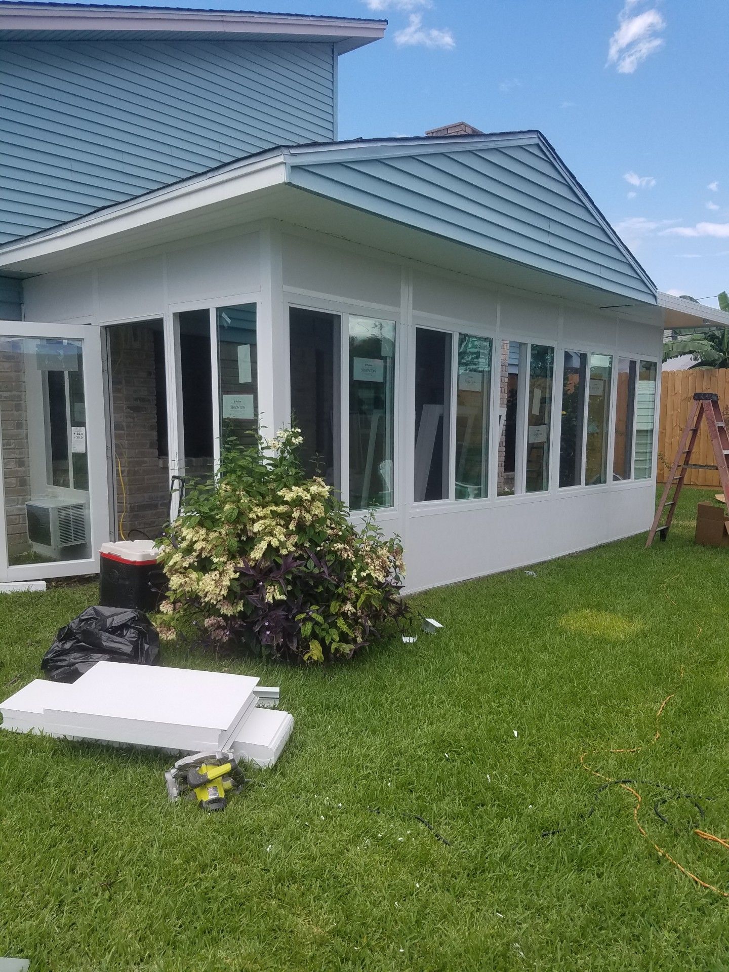 White sunroom addition attached to a light blue house with a green lawn in the foreground.