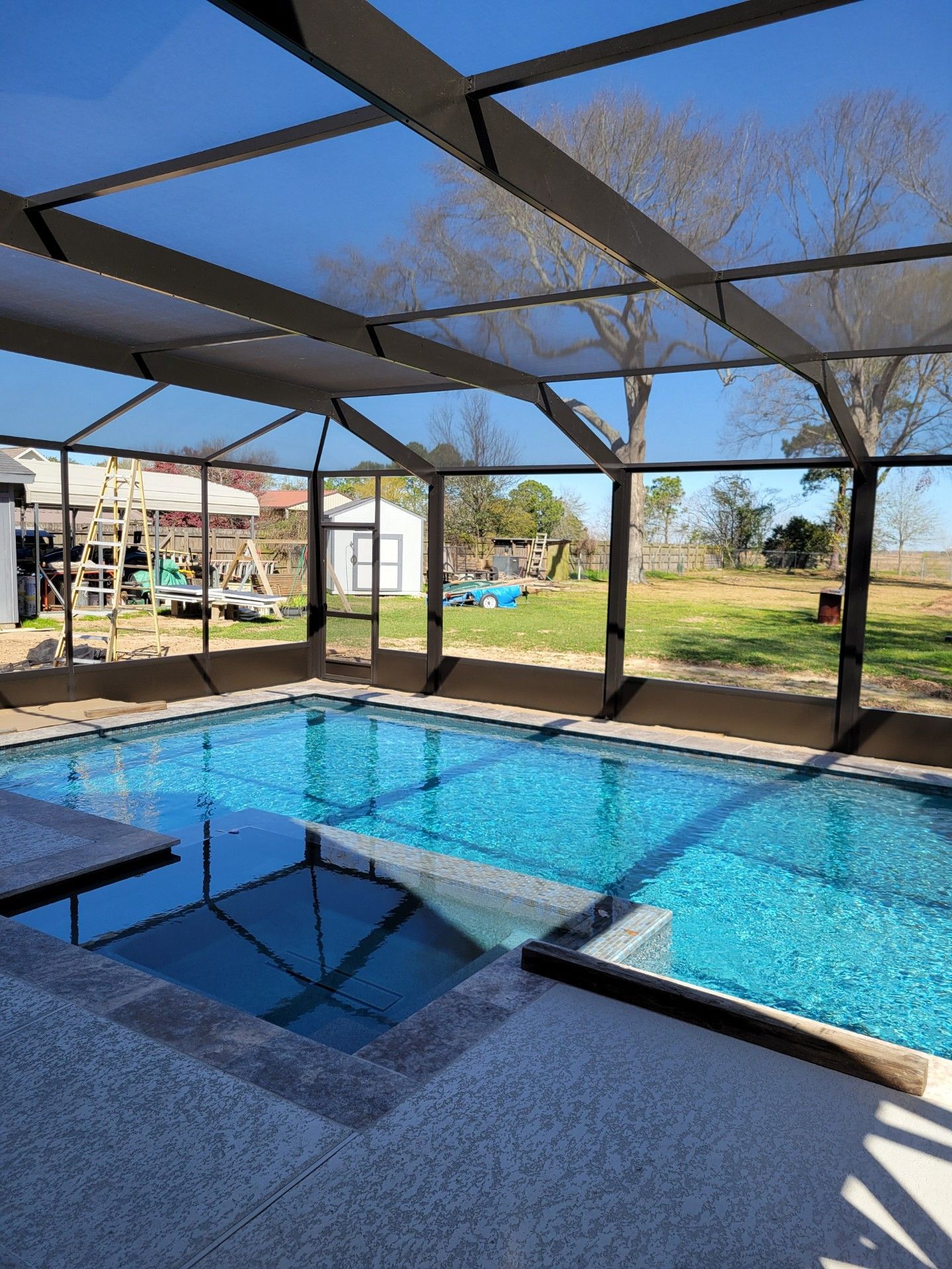 A rectangular swimming pool under a screened enclosure. The pool water is turquoise, and the setting is outdoors on a sunny day.