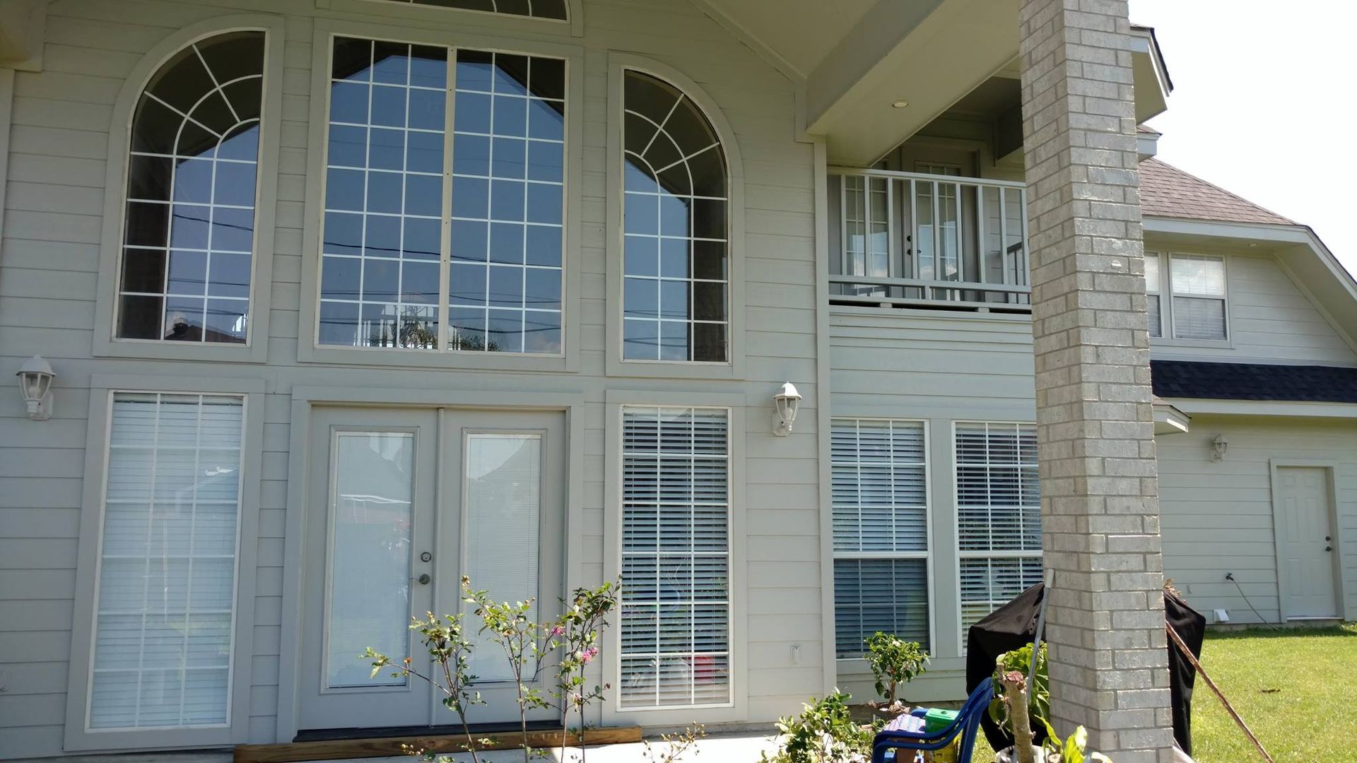 Two-story house with large arched windows and a balcony. The exterior is painted light gray with a brick pillar.