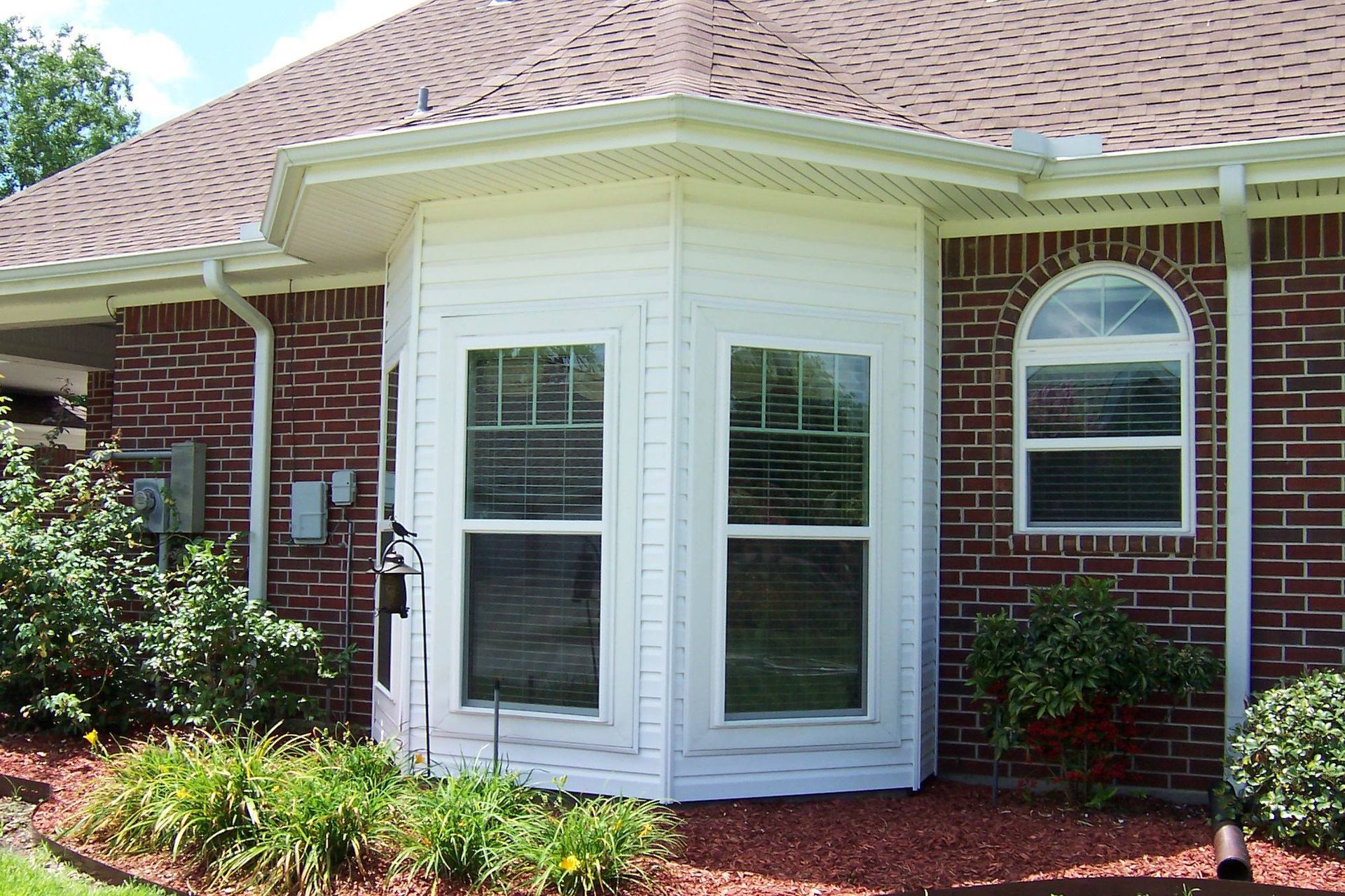 Brick house exterior with white bay window and arched window. Red mulch borders the yard.
