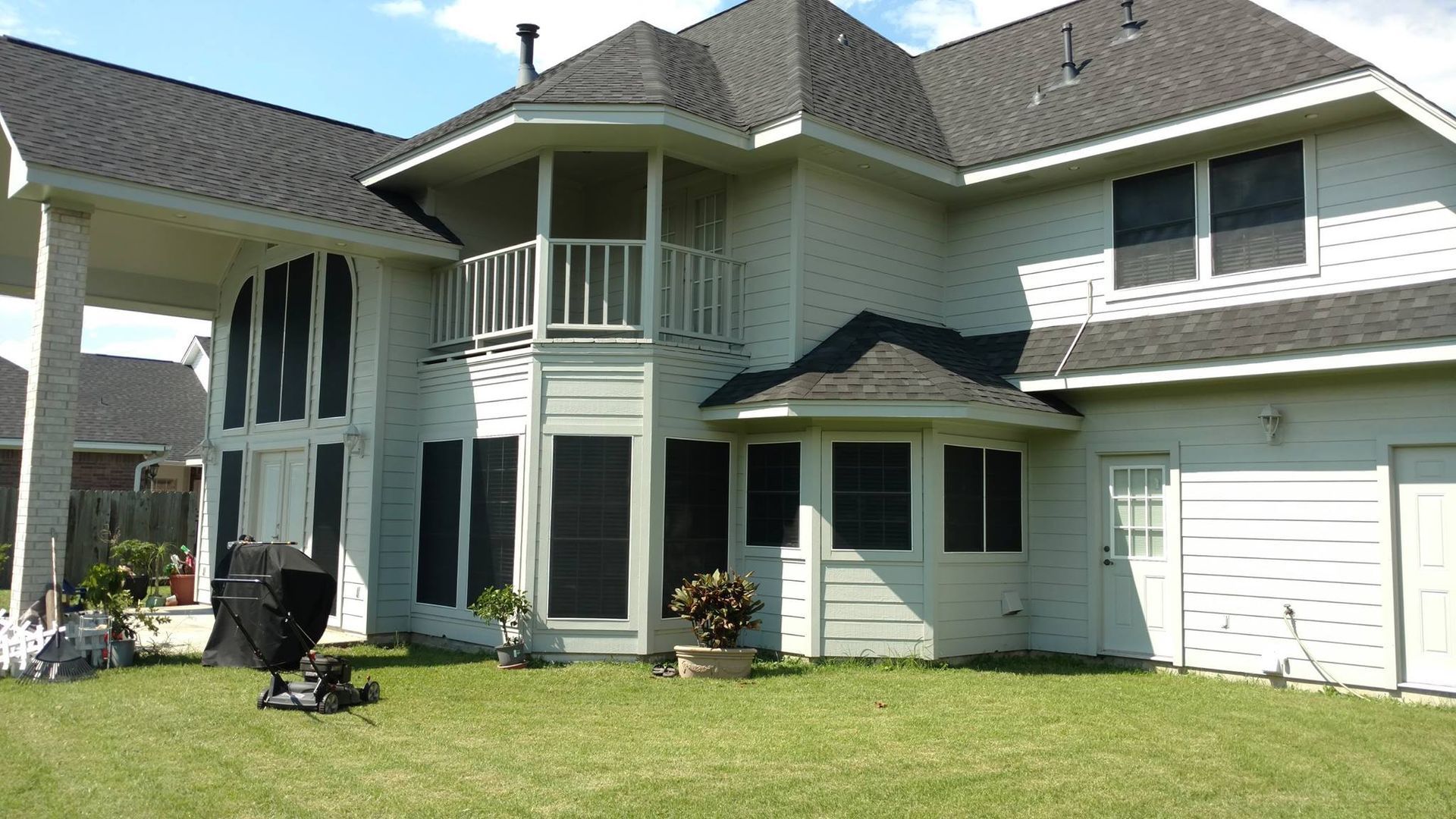Backyard view of a two-story house with a black grill on the green lawn; the house has light-colored siding, black shutters, and a dark gray roof.
