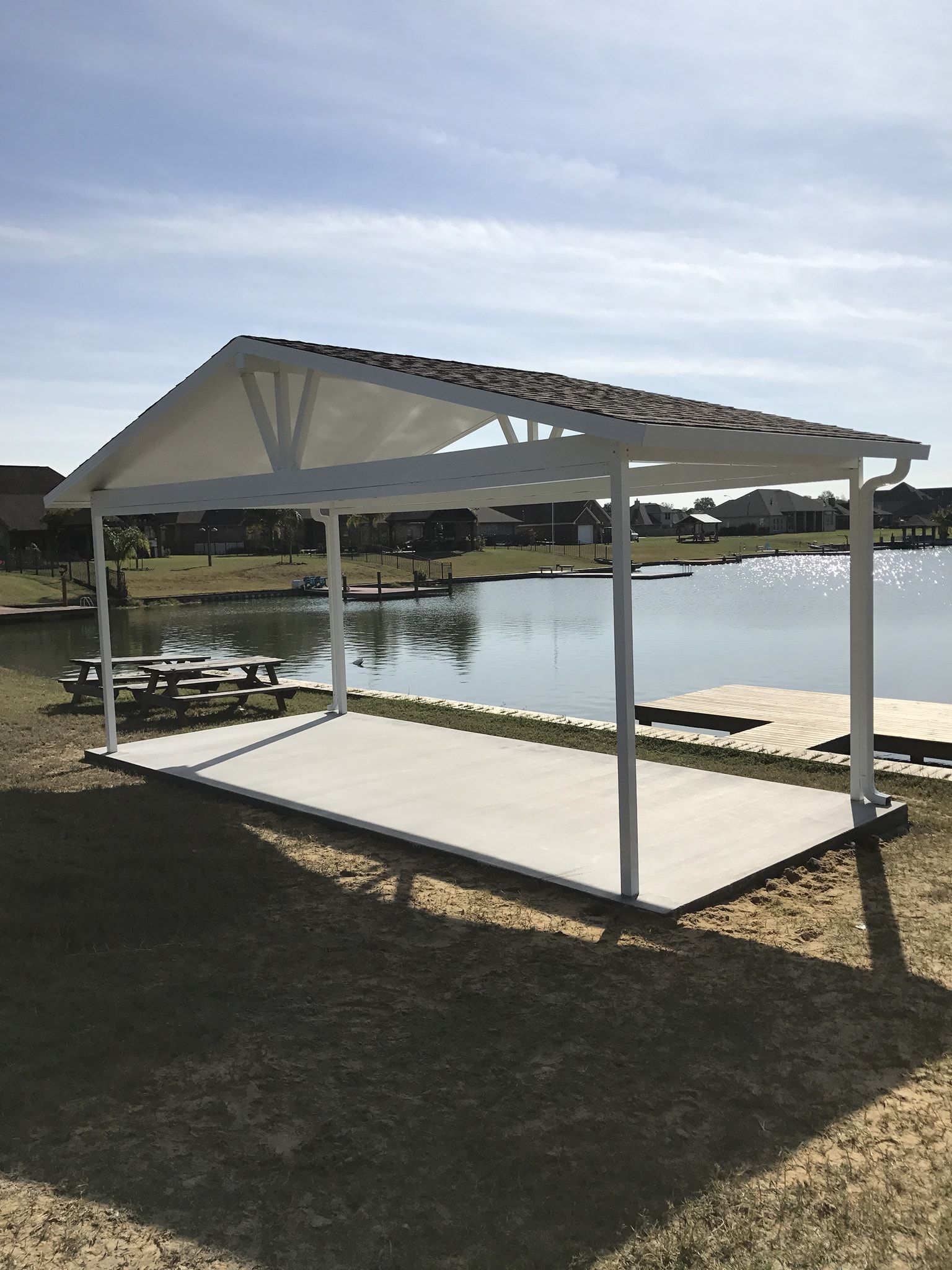 White gazebo with a light-colored roof, overlooking a lake. A picnic table is in the distance.