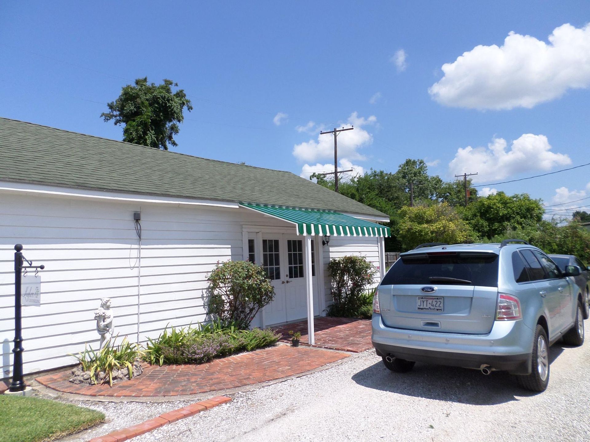 White building with green awning and blue SUV parked in front.