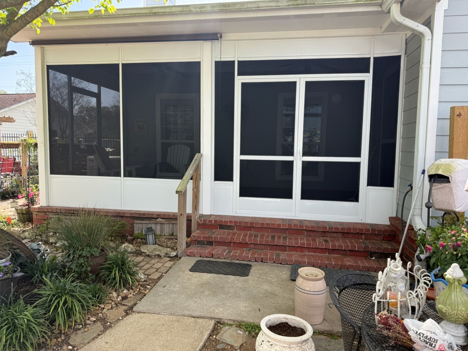 Screened-in porch with white trim, brick steps, black screens, and a small front yard with plants.