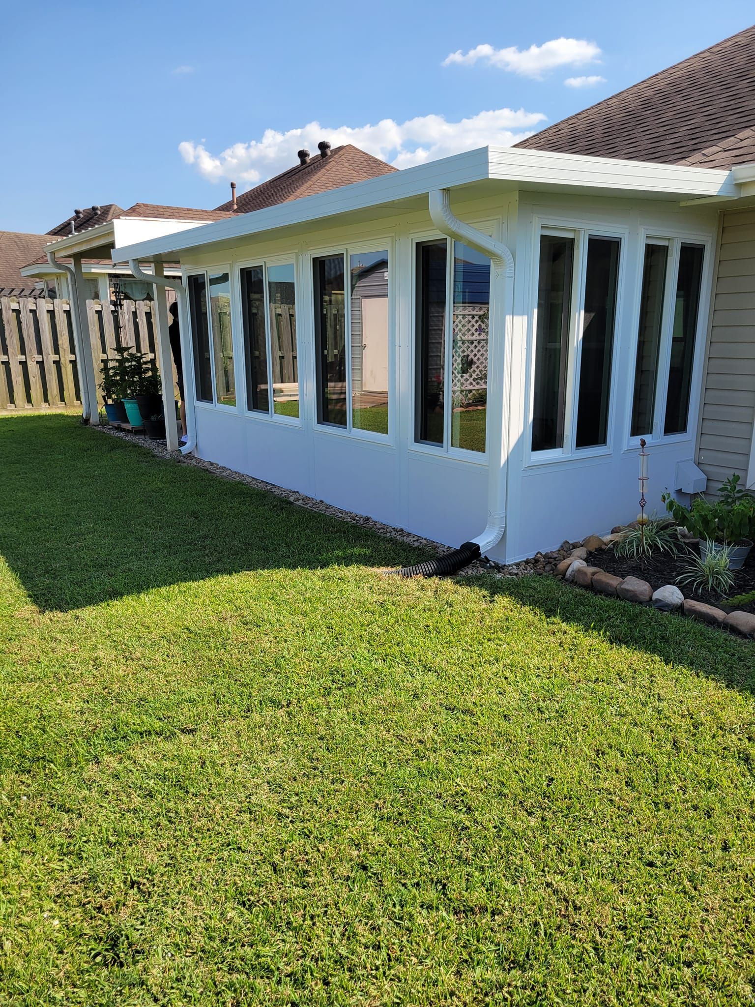 White sunroom with multiple windows attached to a beige house, green grass, and blue sky.