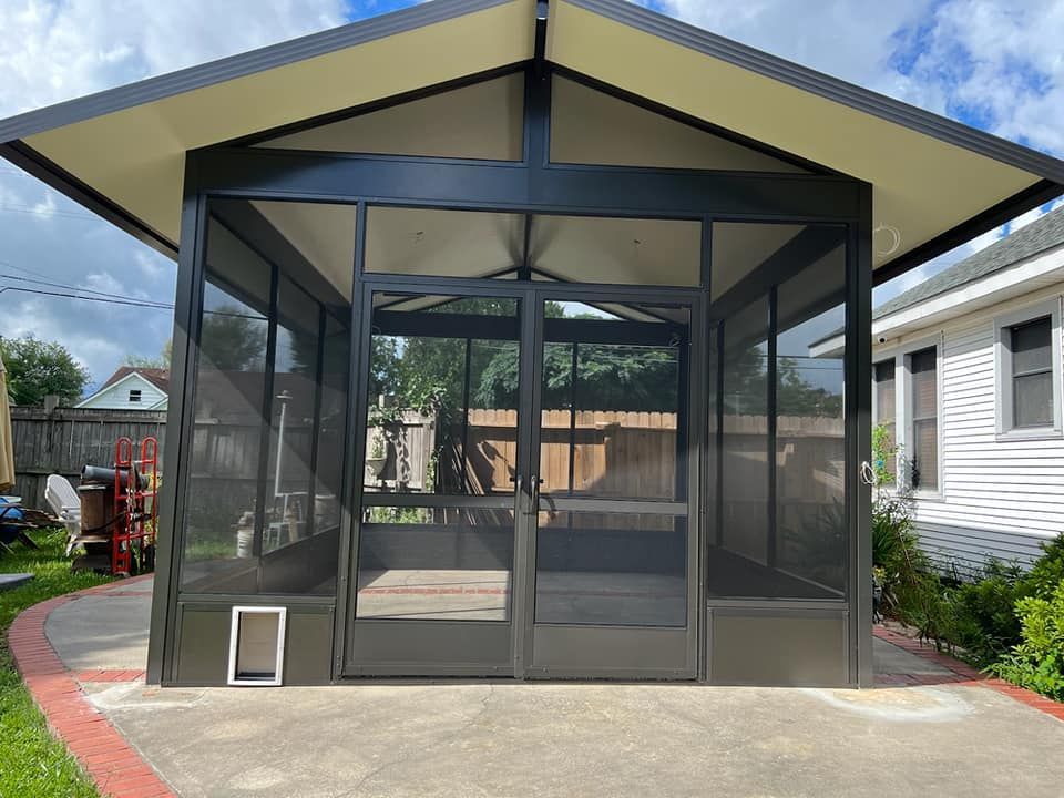 Black screened-in patio with a peaked roof and a door, sitting on a concrete patio.