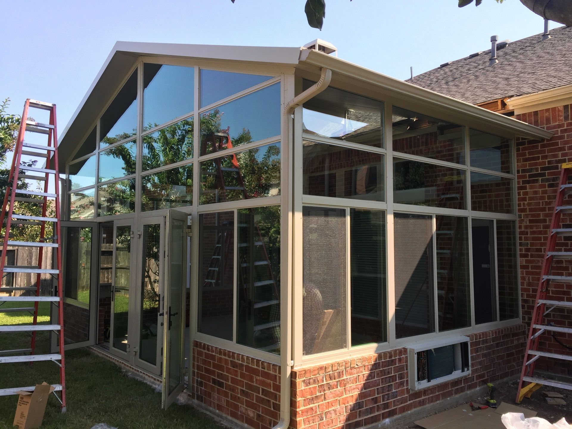 Sunroom addition with large glass windows and a brick base; ladders are present.