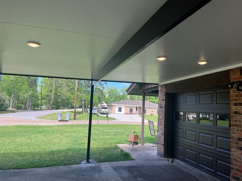 Carport with overhead lighting and a black garage door. Exterior view of a neighborhood.