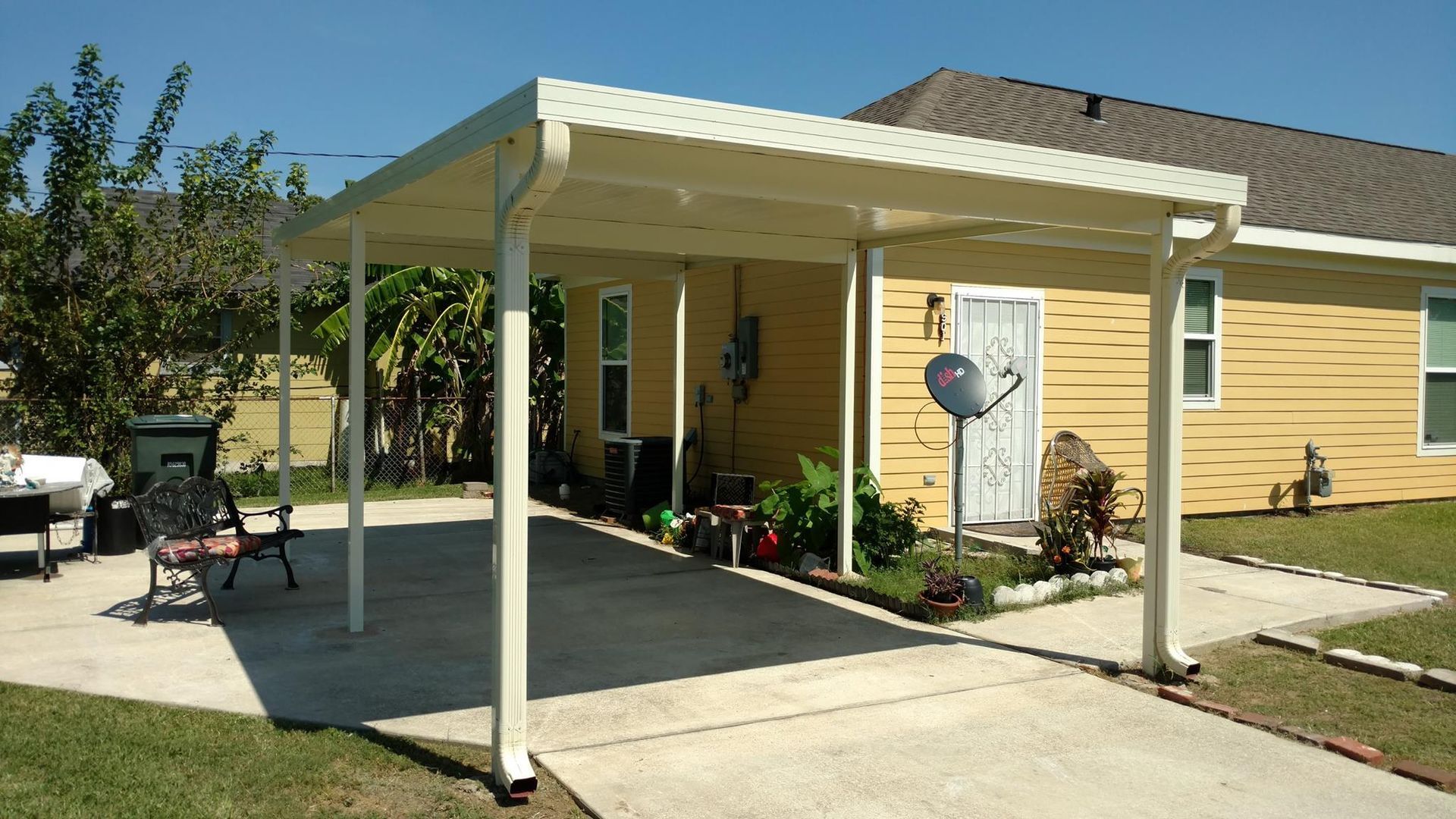 Cream-colored carport attached to a yellow house with a concrete driveway and lawn.
