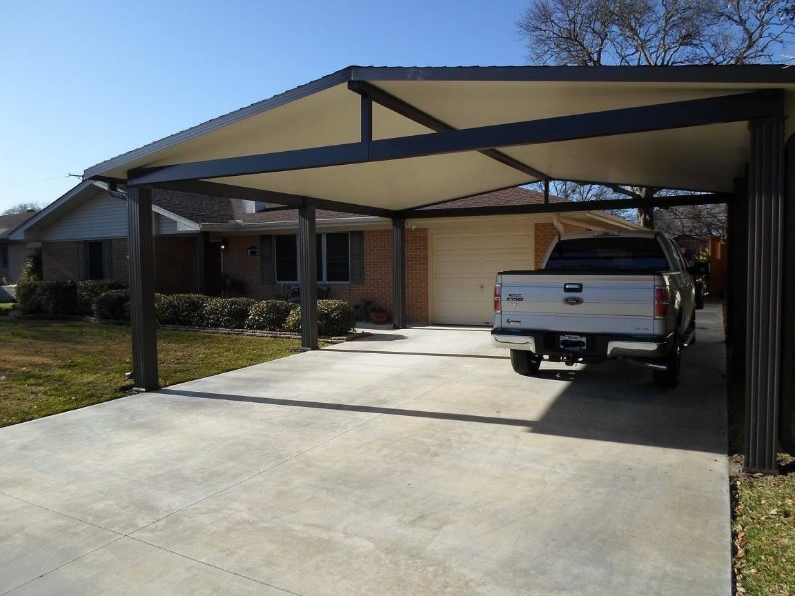 Carport over a concrete driveway with a truck parked underneath, in front of a house.