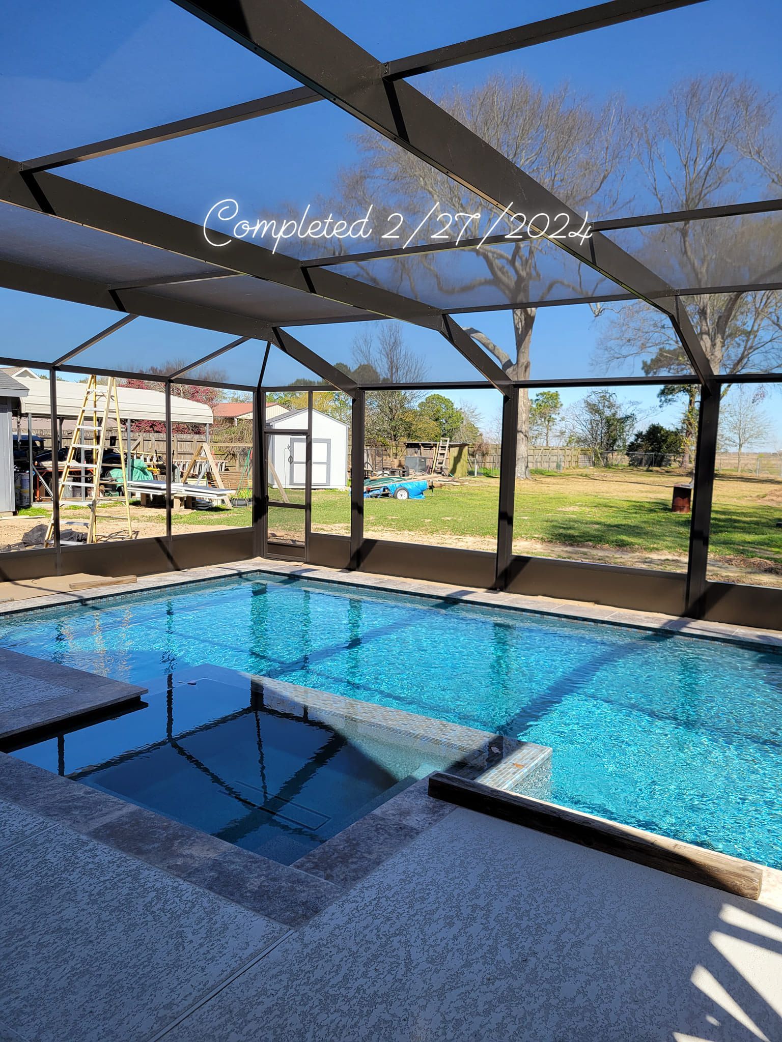 Pool with screened enclosure, blue water, and patio area, completed on 2/27/2022.