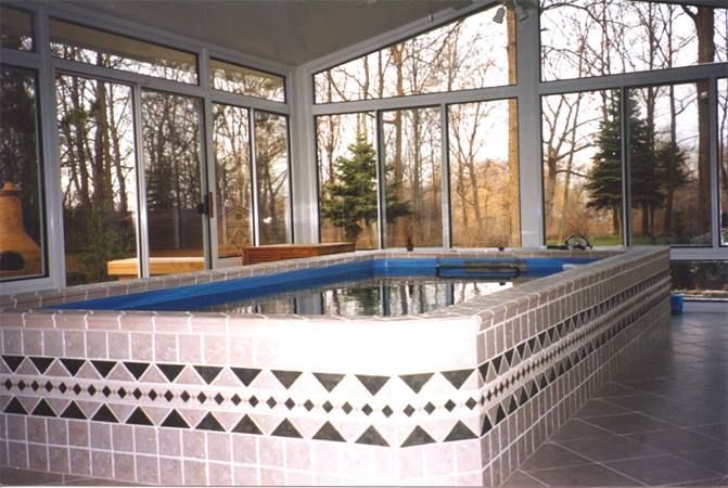 Indoor rectangular pool with tiled surround, large windows, and outdoor trees.