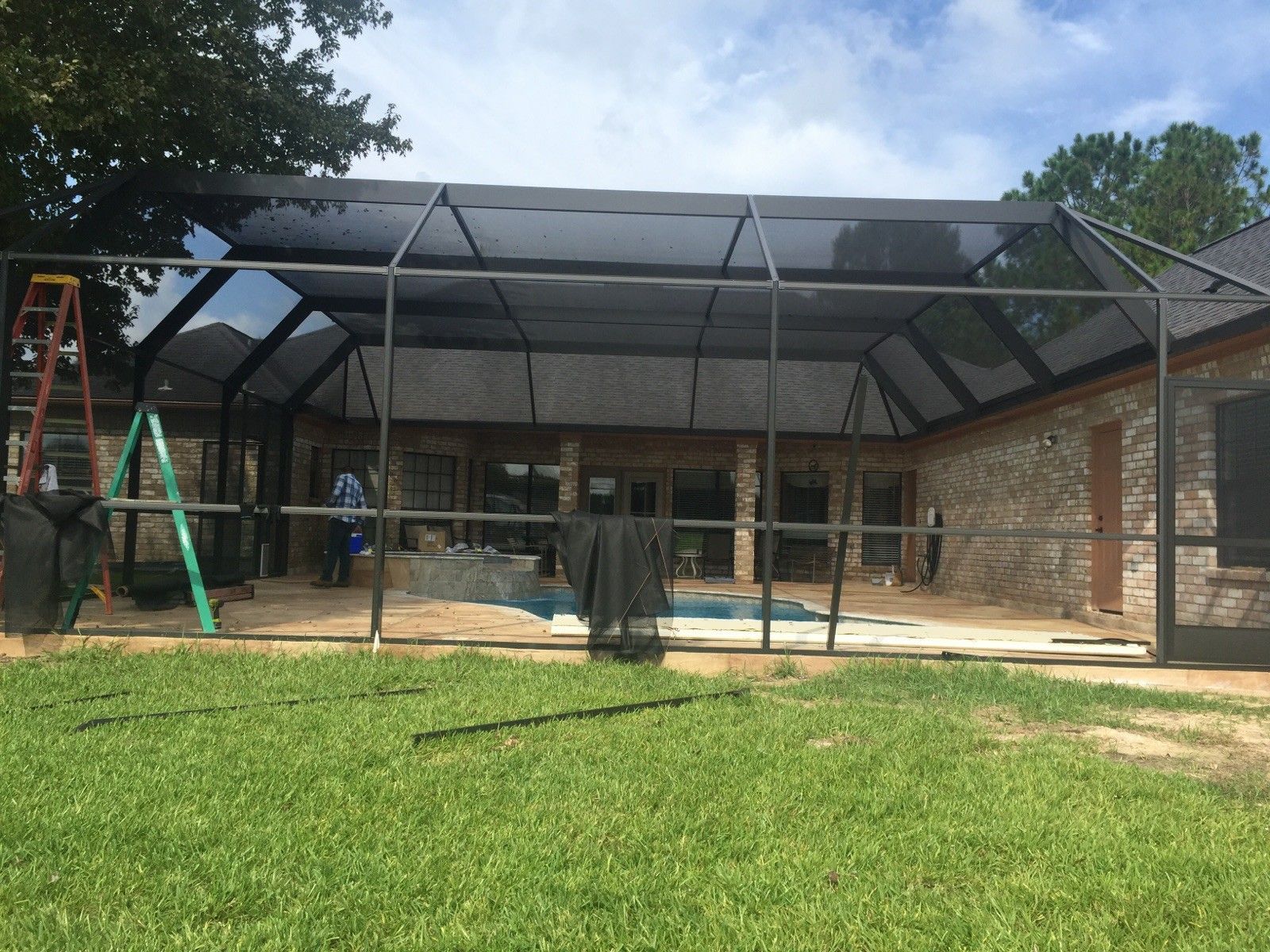 A screened-in pool enclosure with a black frame and a black mesh roof, set behind a green lawn.