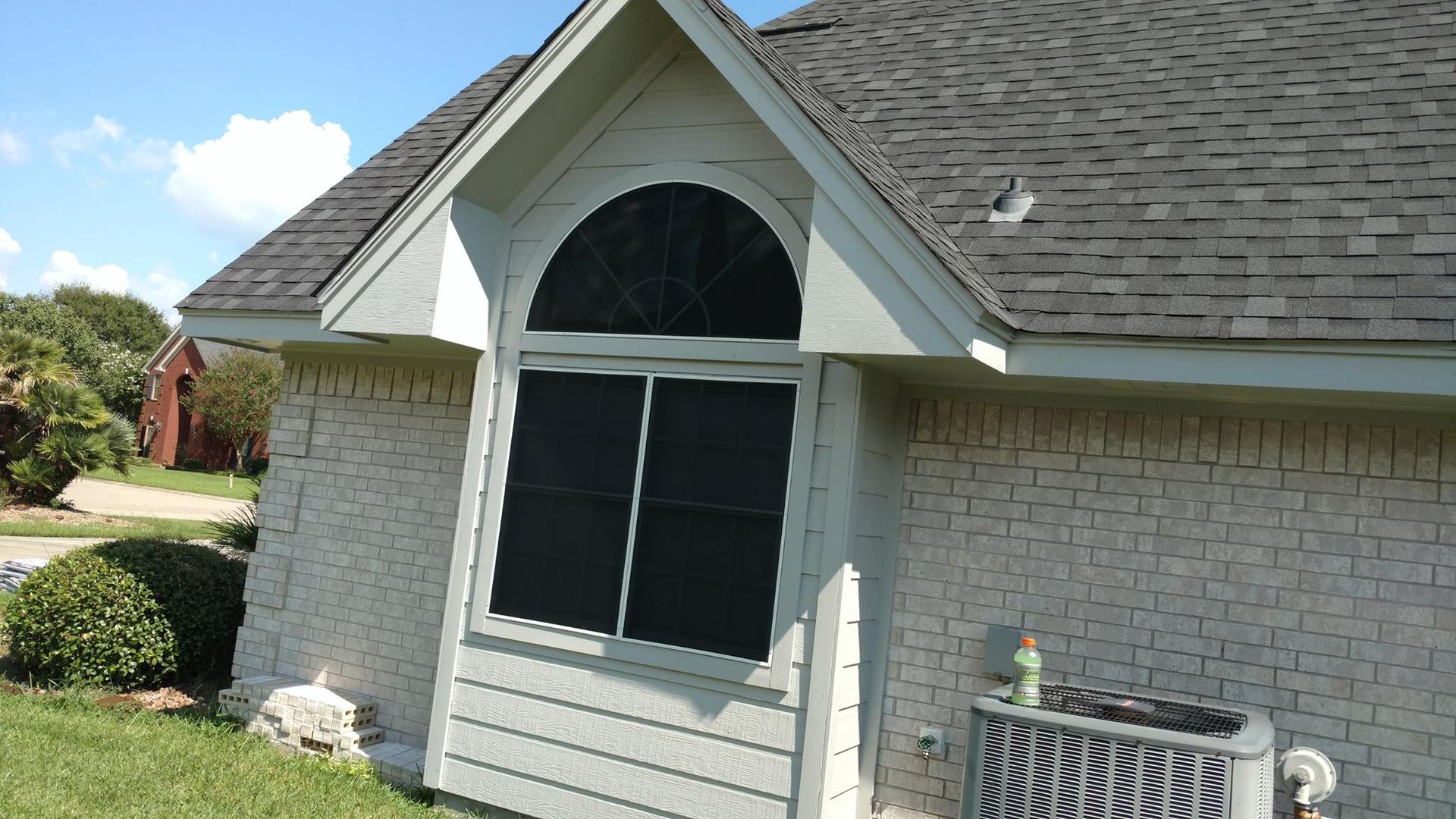Exterior of a brick house with a dark roof and an arched window. An air conditioning unit sits below the window.