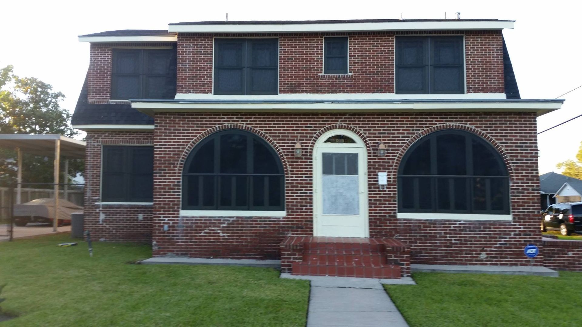 Brick house with arched windows, front porch, and a second-story dormer, set on a green lawn.