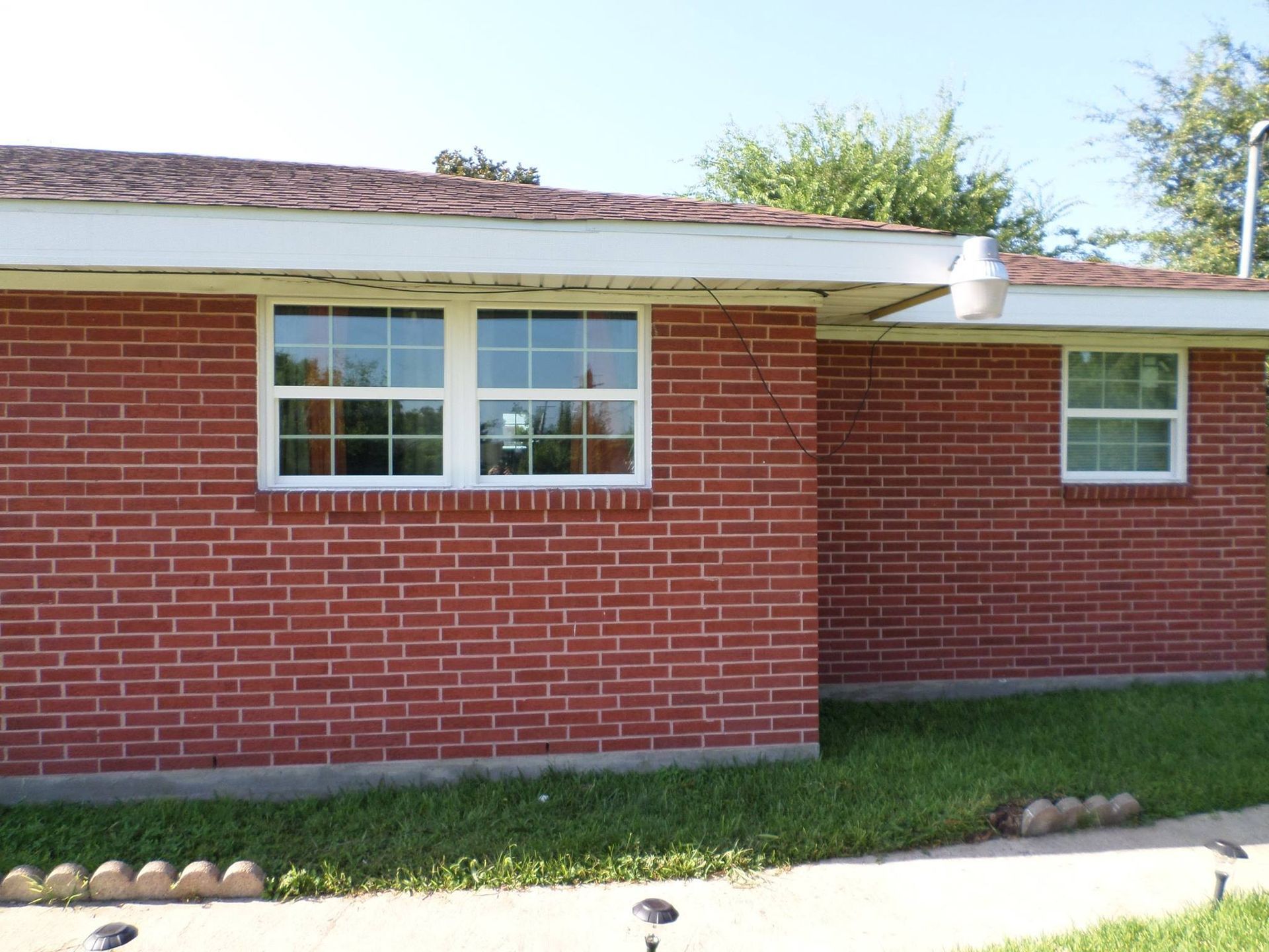 Red brick house with white-framed windows, green grass, and a clear blue sky.