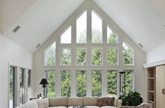 Living room with large, multi-pane windows and a white, vaulted ceiling. A cream-colored sofa sits in front of the windows.