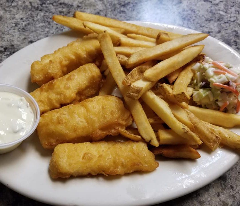 A plate of fish and french fries with coleslaw and sour cream