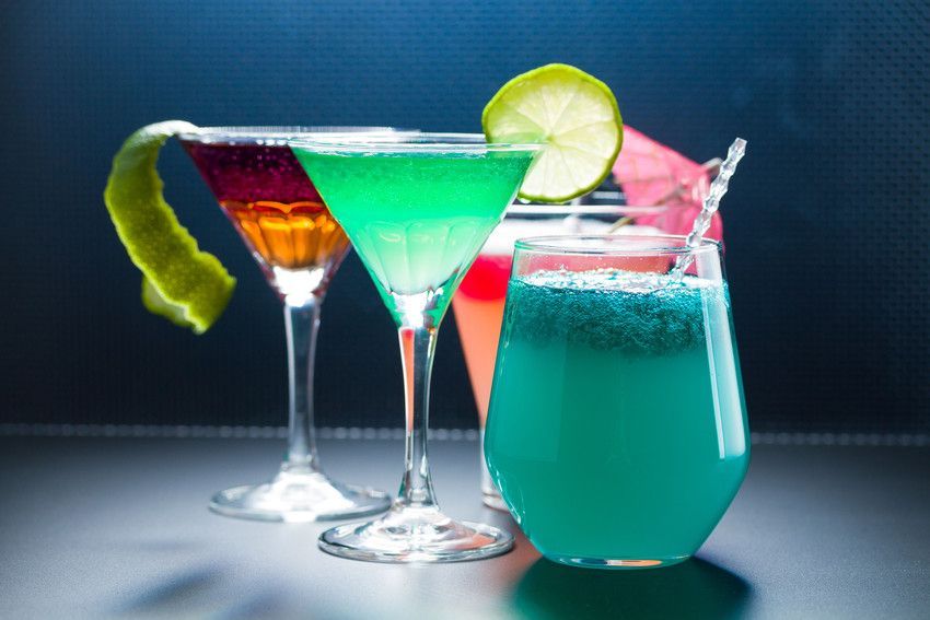 Four different colored cocktails are lined up on a table.