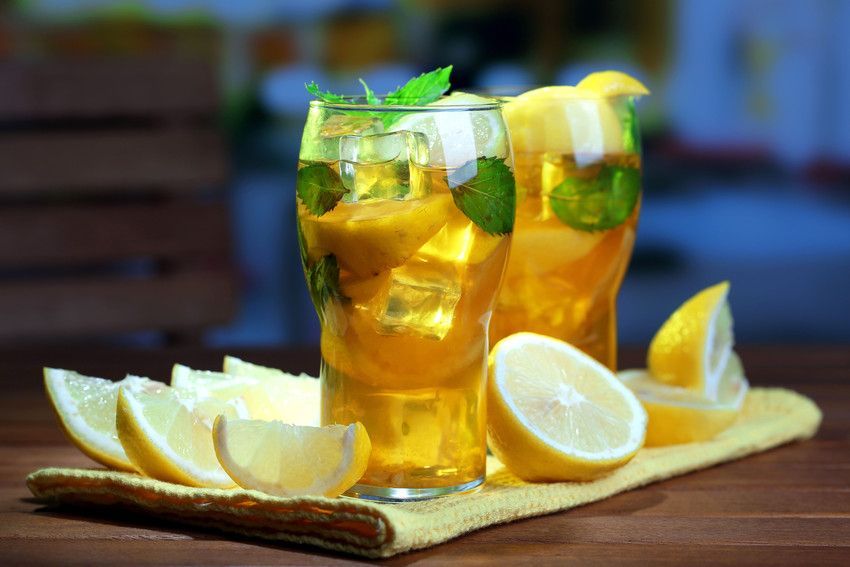 Two glasses of iced tea with lemons and mint on a wooden table.
