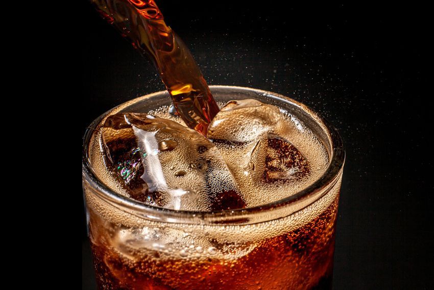 A glass of cola is being poured into a glass with ice cubes.