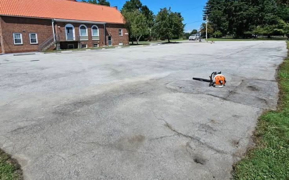 Empty asphalt parking lot beside a brick building with a red roof under a clear blue sky.