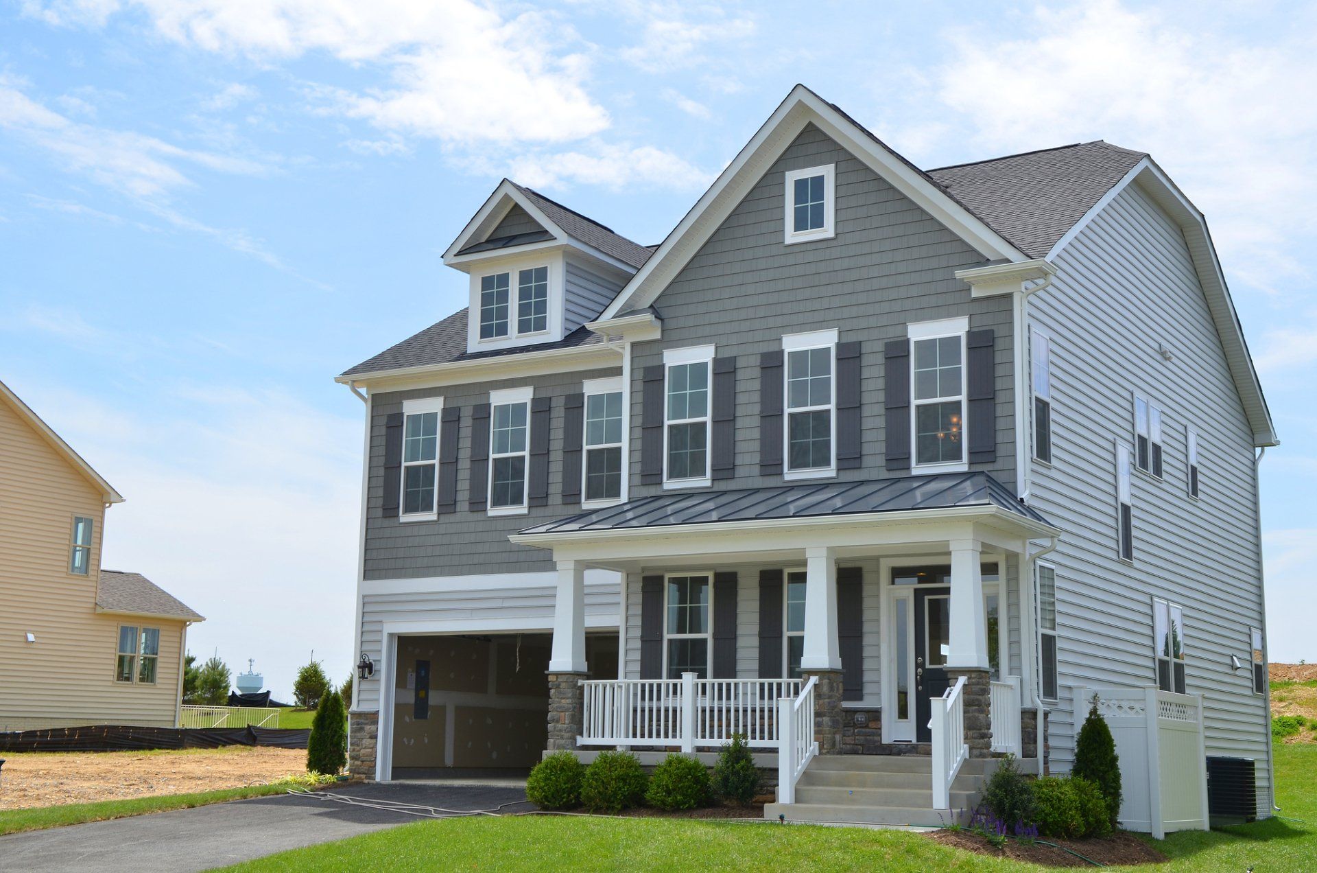 A grey two-story house with a front porch, garage, and gabled roof under a bright blue sky.