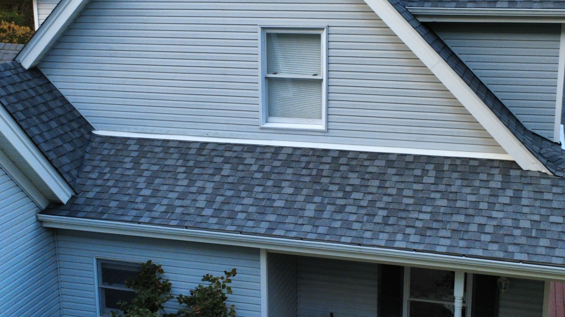 A light gray, multi-story house with dark asphalt shingles and a large window centered on the upper level.