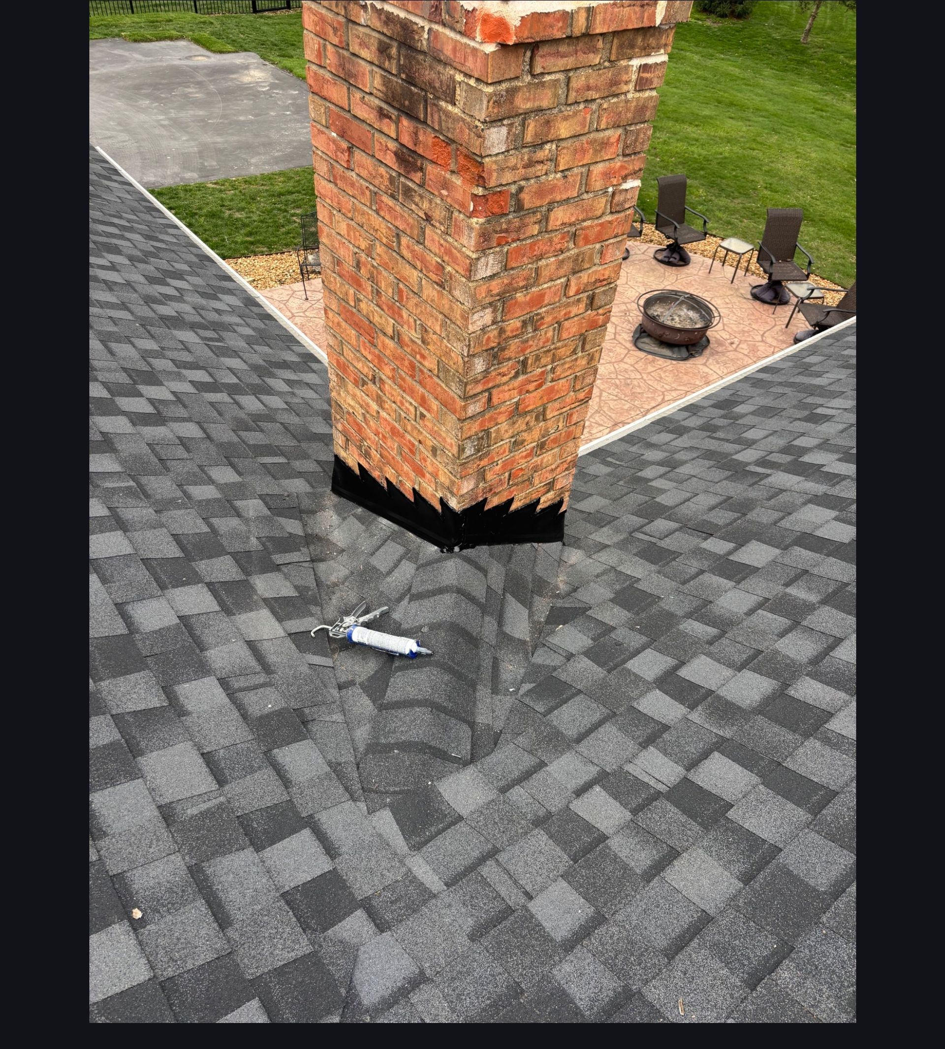 Brick column on gray pavers beside a small landscaped area with black fixtures.