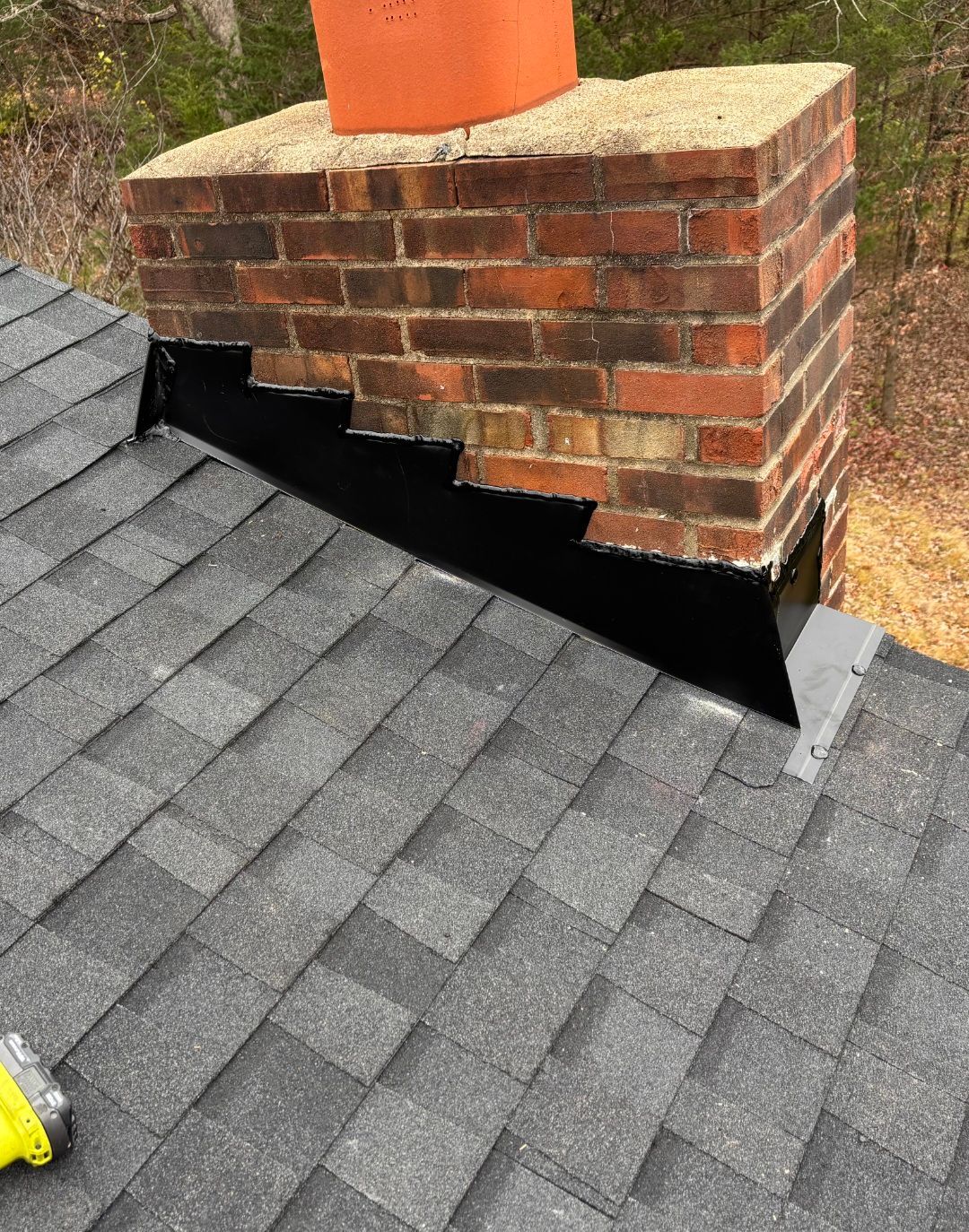 Brick chimney with black flashing on a gray shingled roof, viewed close up.