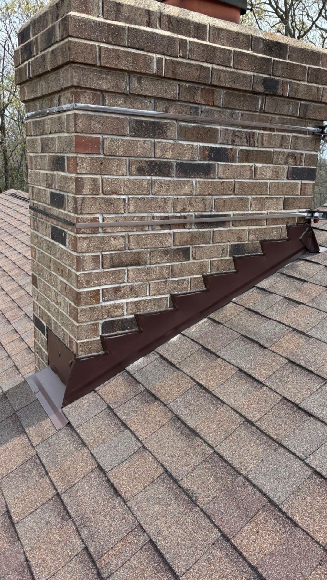 Brick chimney with a brown metal flashing base on a shingled roof