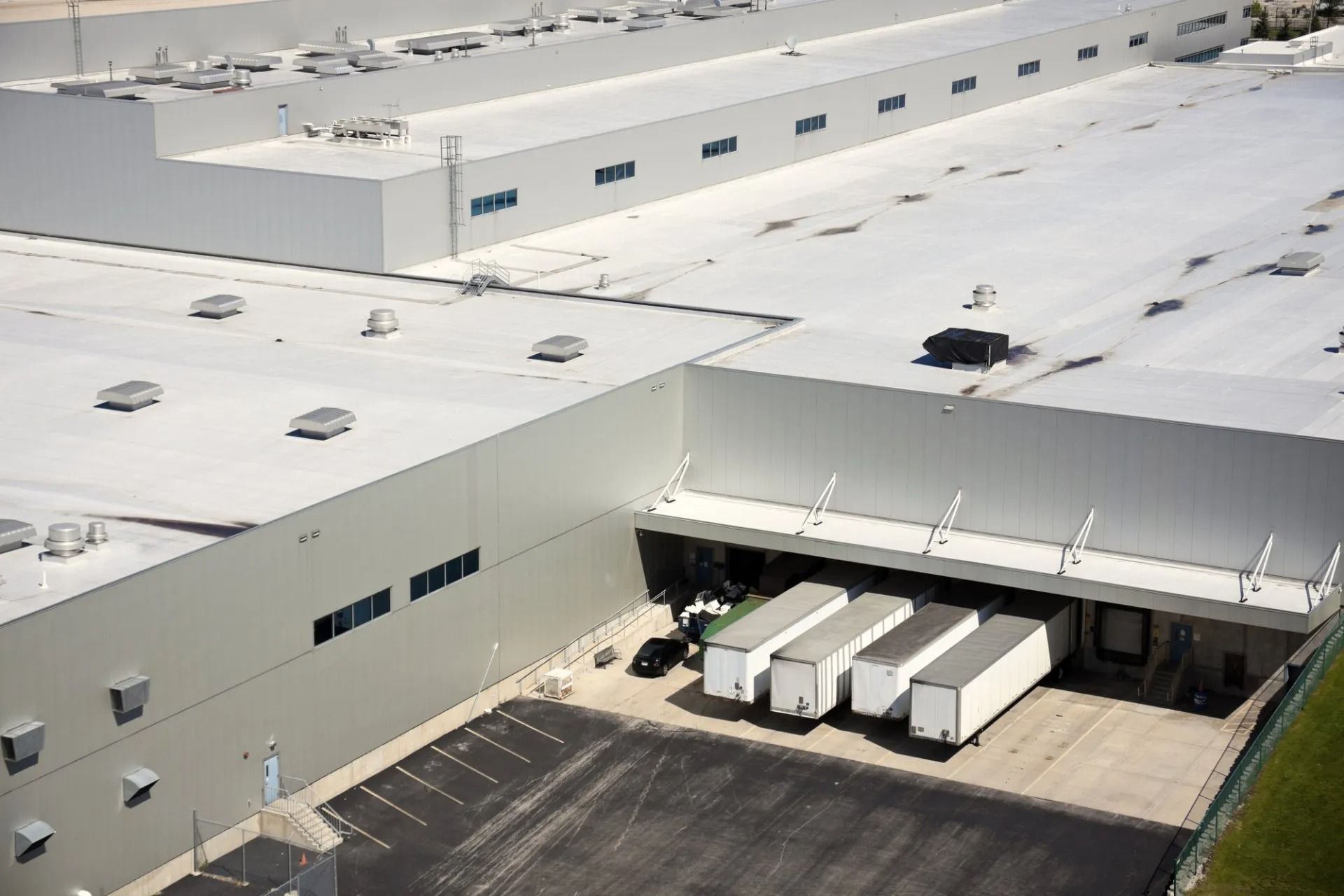 An aerial view of a large industrial warehouse with four white semi-trailers docked at the loading bays.