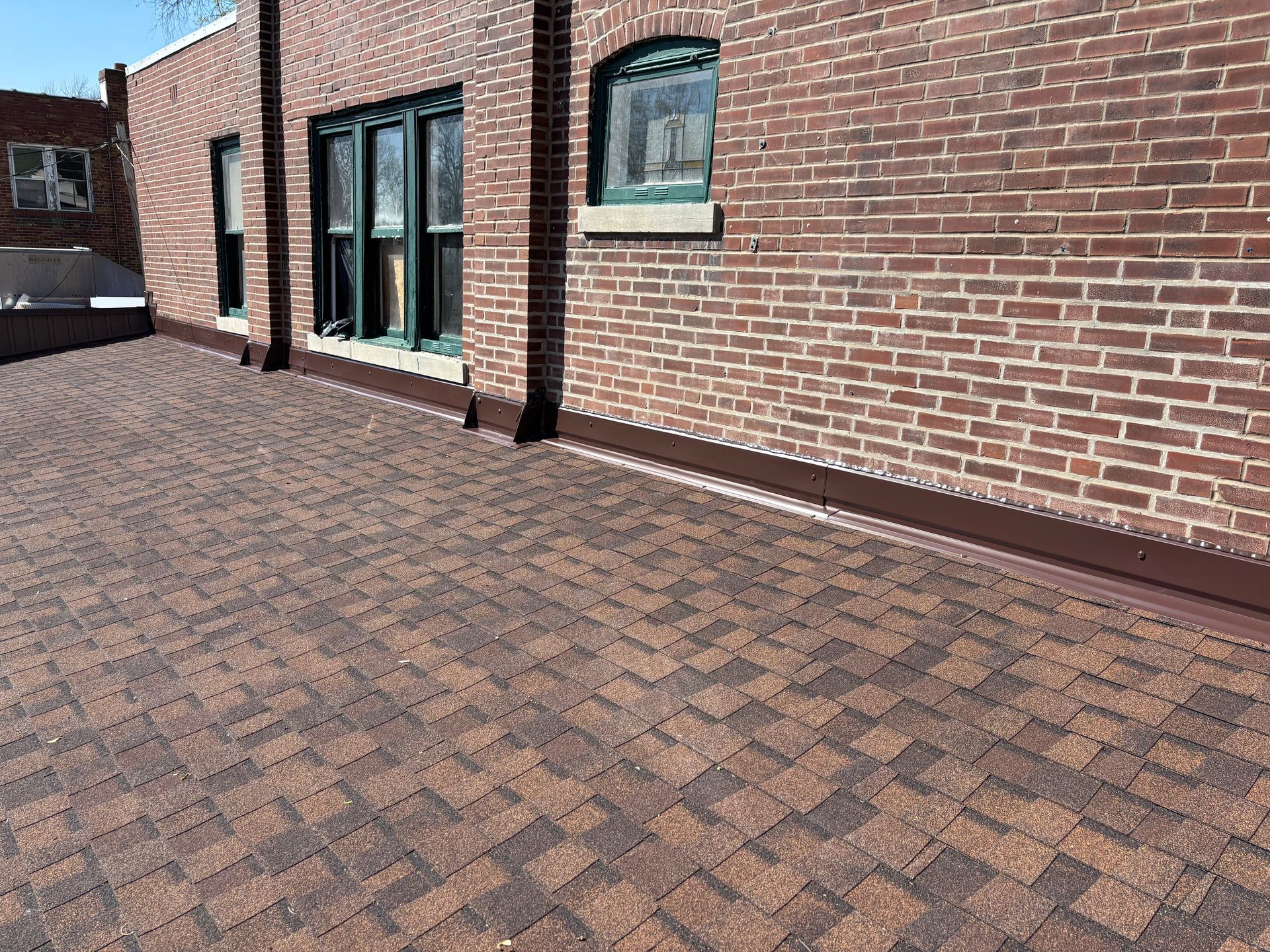 A flat, dark-red brick roof patio with a decorative brown and tan herringbone paver pattern, adjacent to a brick wall.