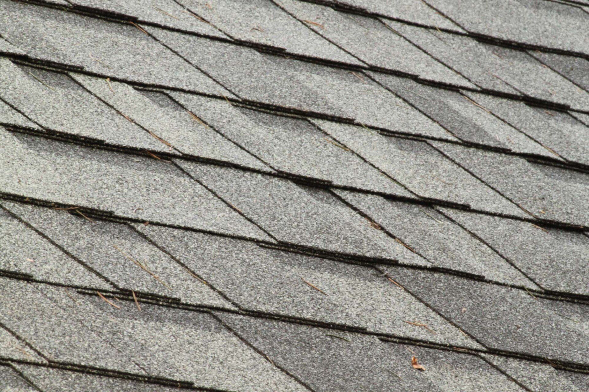 A close-up view of overlapping gray asphalt roof shingles arranged in a diagonal pattern.