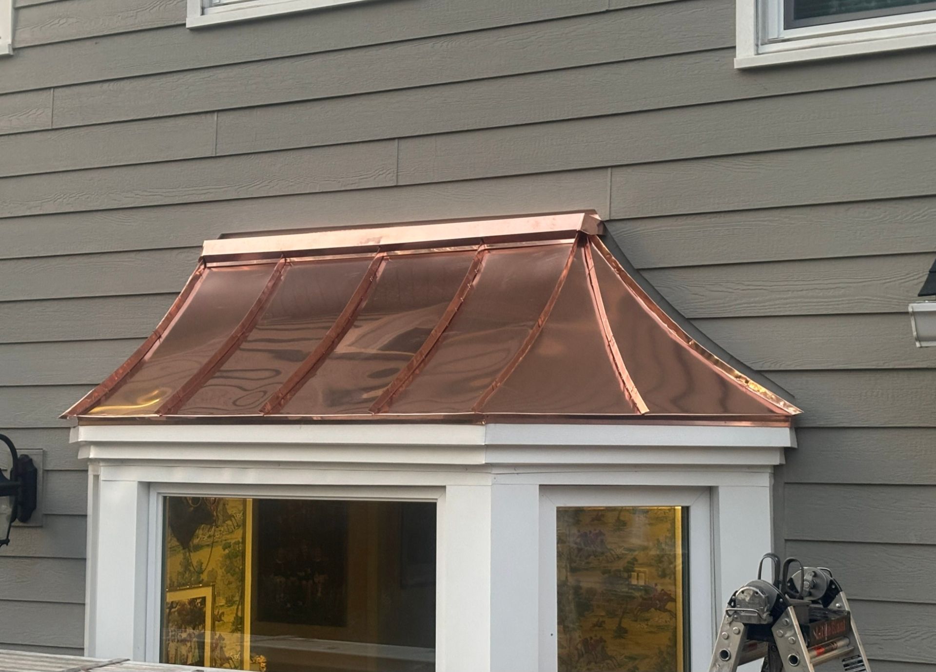 Copper-colored metal roof over a white windowed porch on a gray house facade