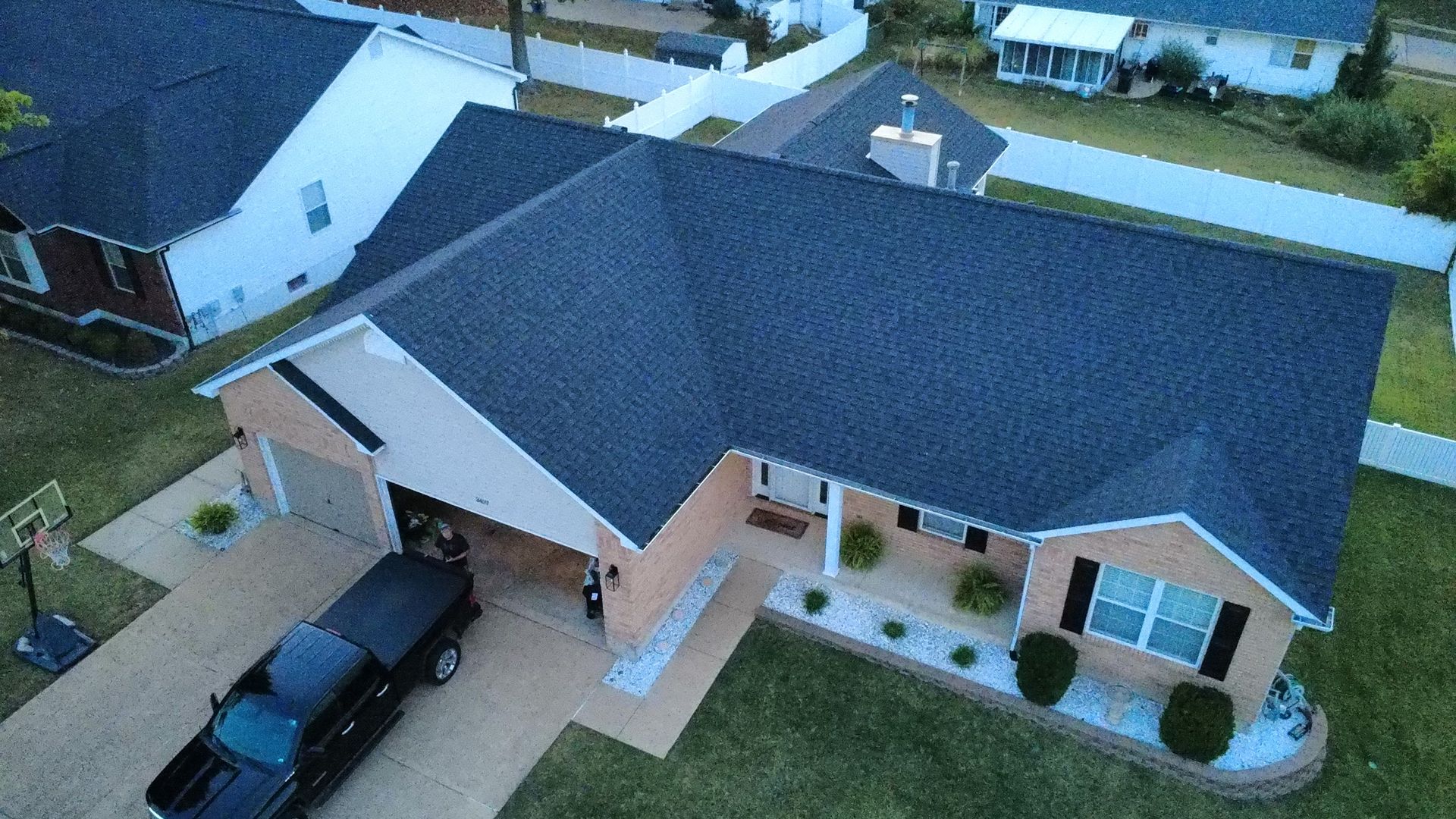 An aerial view of a brick house with a dark shingled roof, a front porch, and a black pickup truck parked in the driveway.