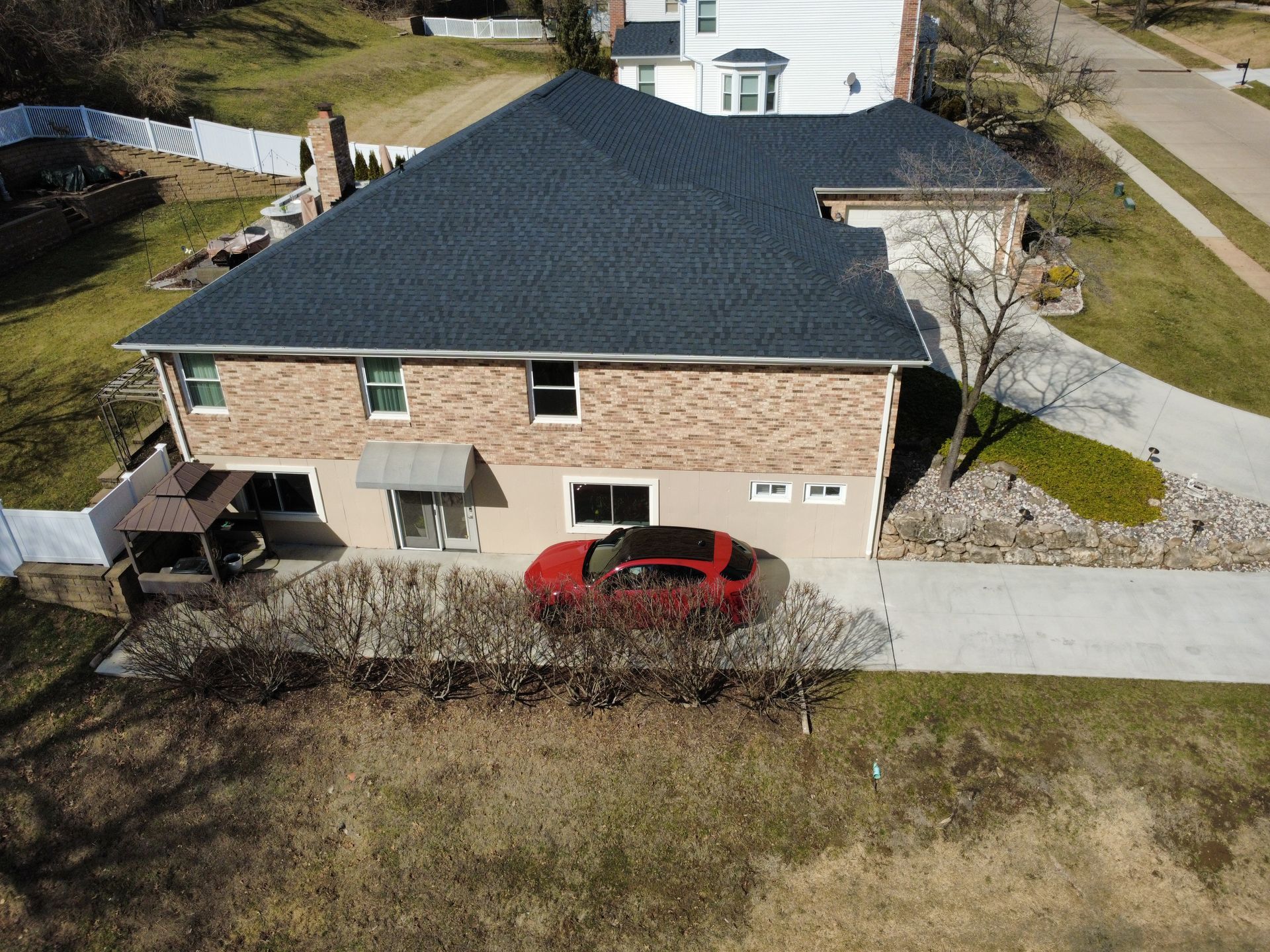 An aerial view of a tan, two-story brick house with a dark roof and a red car parked in the driveway.