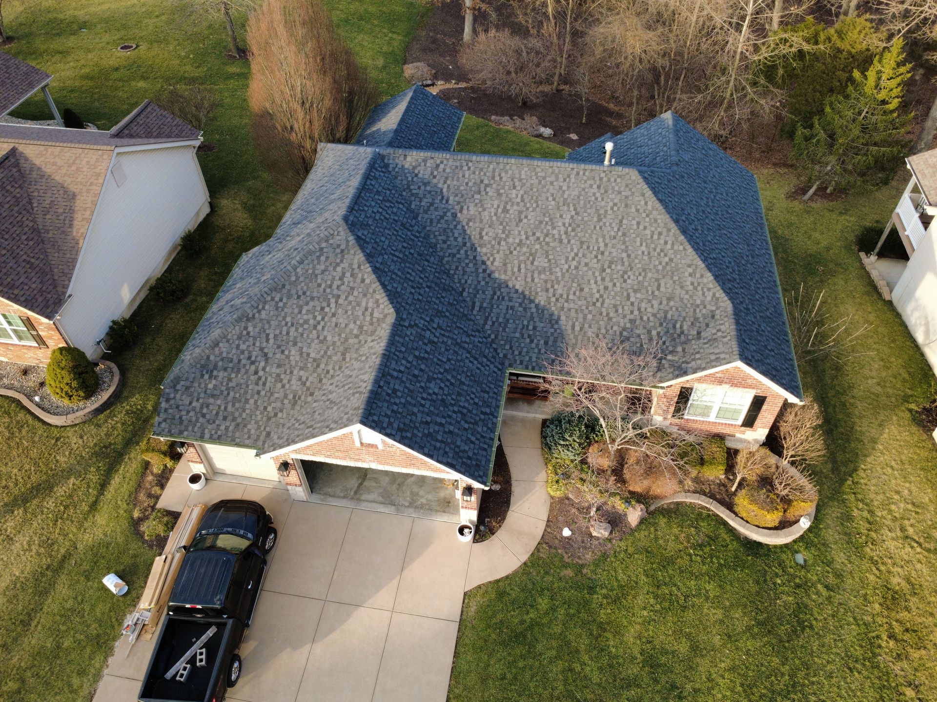 Aerial view of a residential house with a dark gray shingled roof, a concrete driveway, and a black truck parked outside.